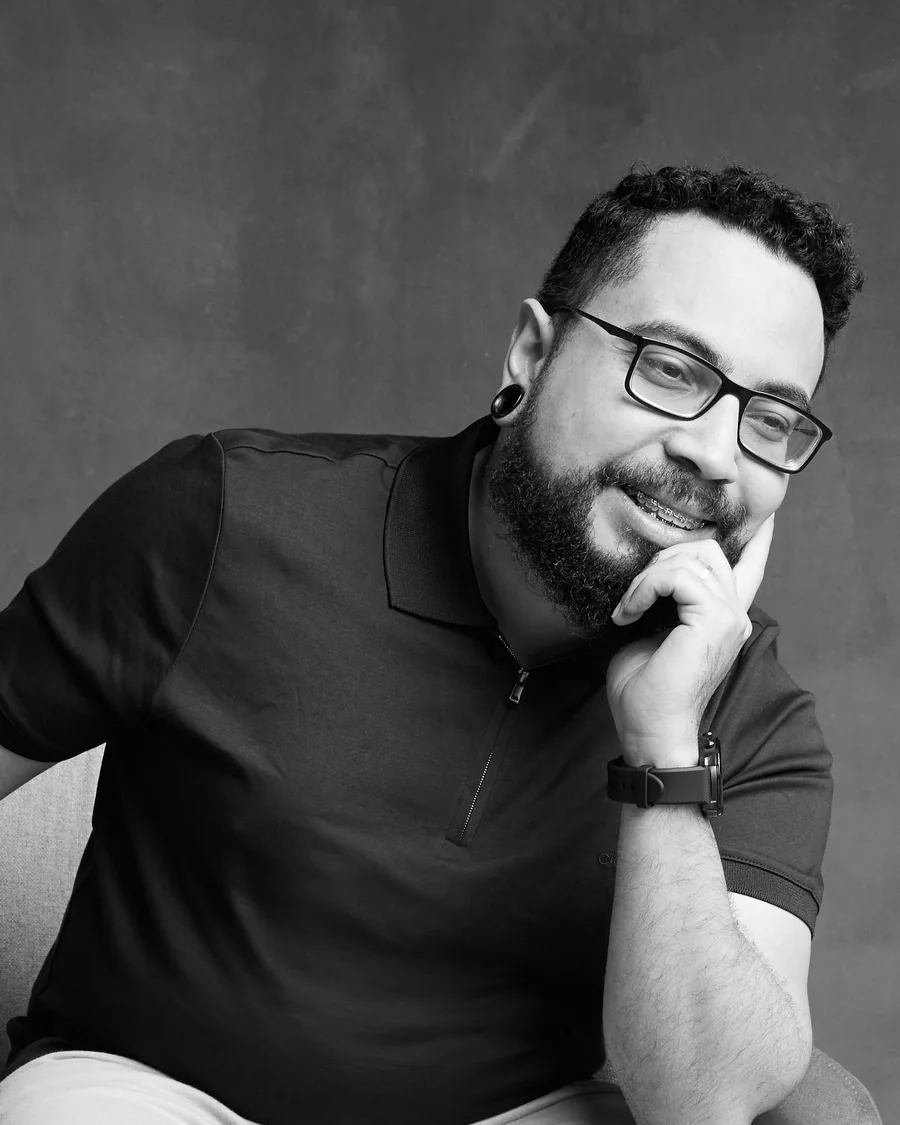 Felipe Renan Santos, homem de barba e óculos, sentado com a mão apoiada no queixo, olhando para a câmera